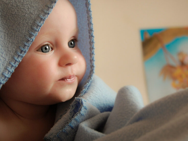 Baby liegt in einer Decke und schaut neugierig in die Kamera.