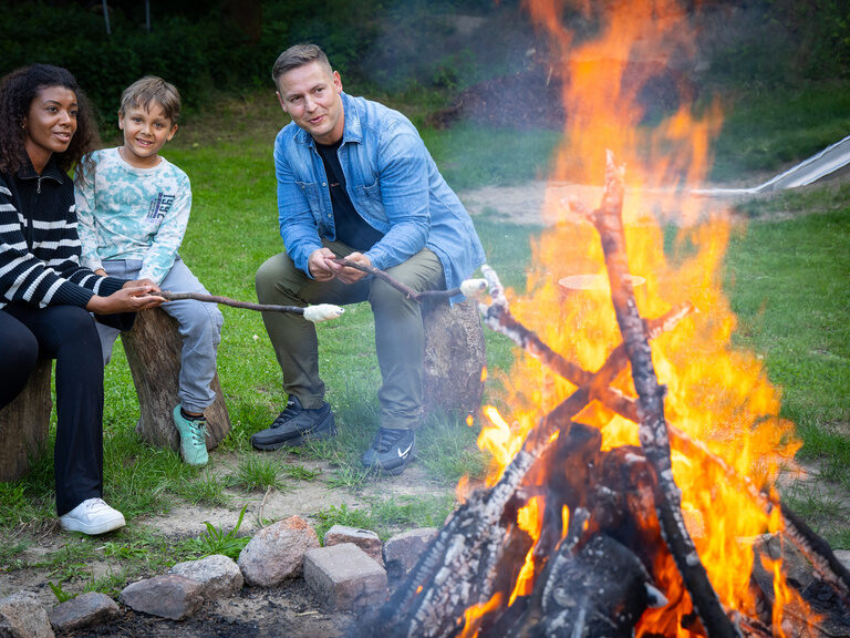 Familie sitzt zusammen am Lagerfeuer und genießt die Wärme