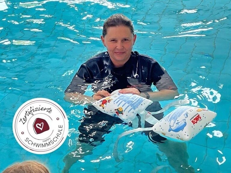 Frau mit Schwimmflügel in der Hand beim Schwimmkurs für Kinder