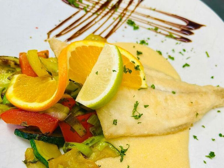 Hauptgericht mit Fisch und Zitronenscheibe auf einem weißen Teller