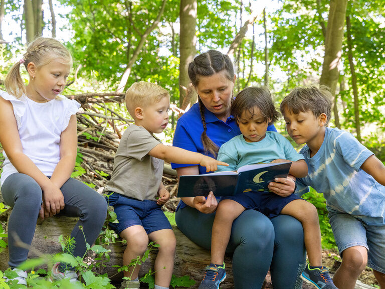 Betreuerin liest Kindern im Wald eine Geschichte vor