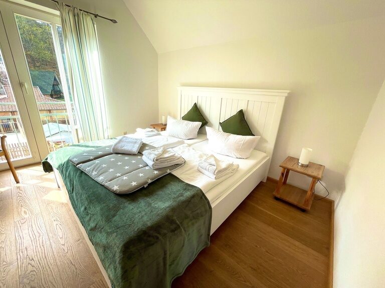 Gemütliches Schlafzimmer mit Doppelbett, grüner Bettwäsche und großen Fenstern.