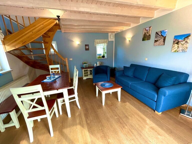 Wohnzimmer mit blauer Couch, Holzboden und Treppe in einer Ferienwohnung im Family Club Harz.