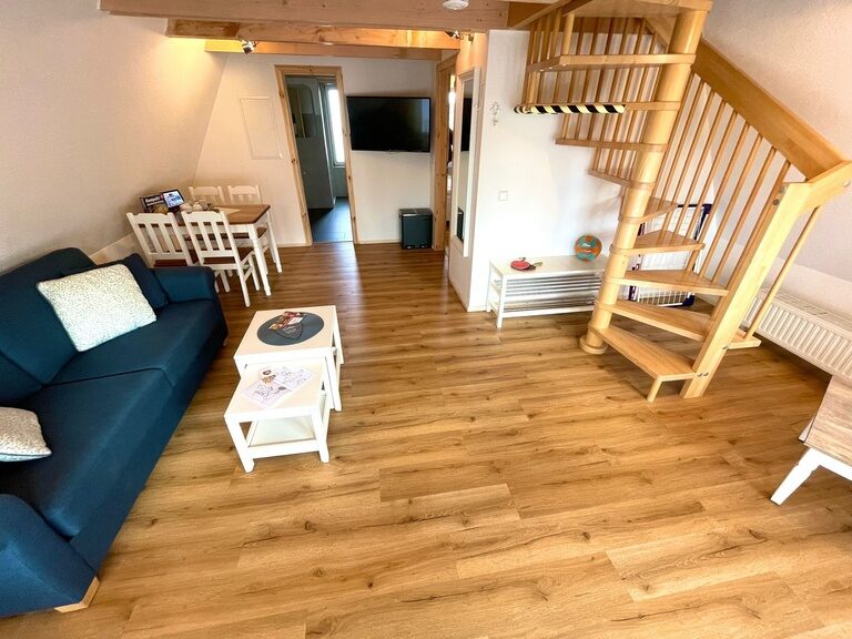 Wohnzimmer mit blauer Couch, Holzboden und Treppe in einer Ferienwohnung im Family Club Harz